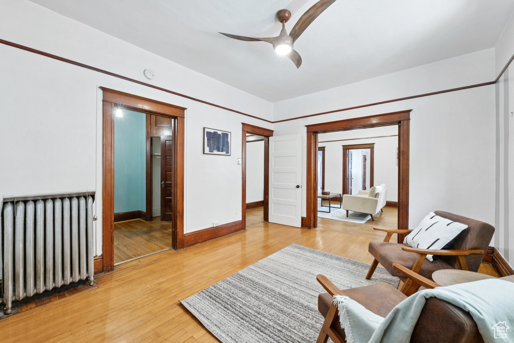 Living area with radiator heating unit, a ceiling fan, and light wood-style floors