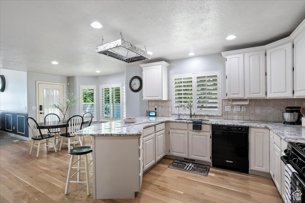 Kitchen with black appliances, a peninsula, white cabinets, light wood finished floors, and recessed lighting