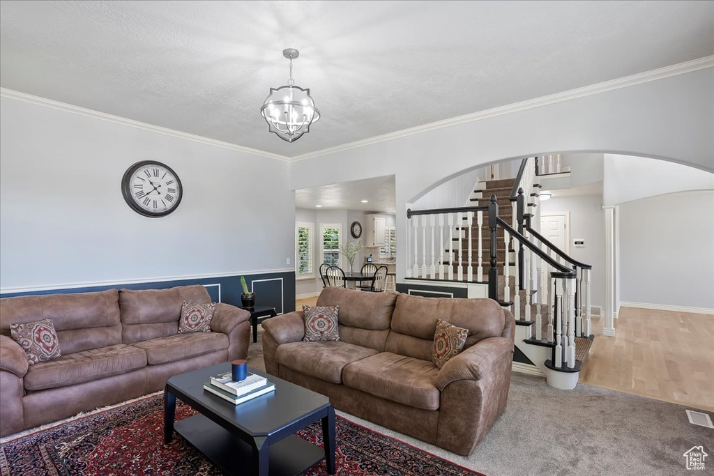Living room featuring stairway, a chandelier, arched walkways, and ornamental molding