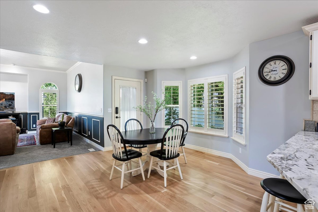 Dining space with light wood-style flooring, recessed lighting, ornamental molding, and a wainscoted wall