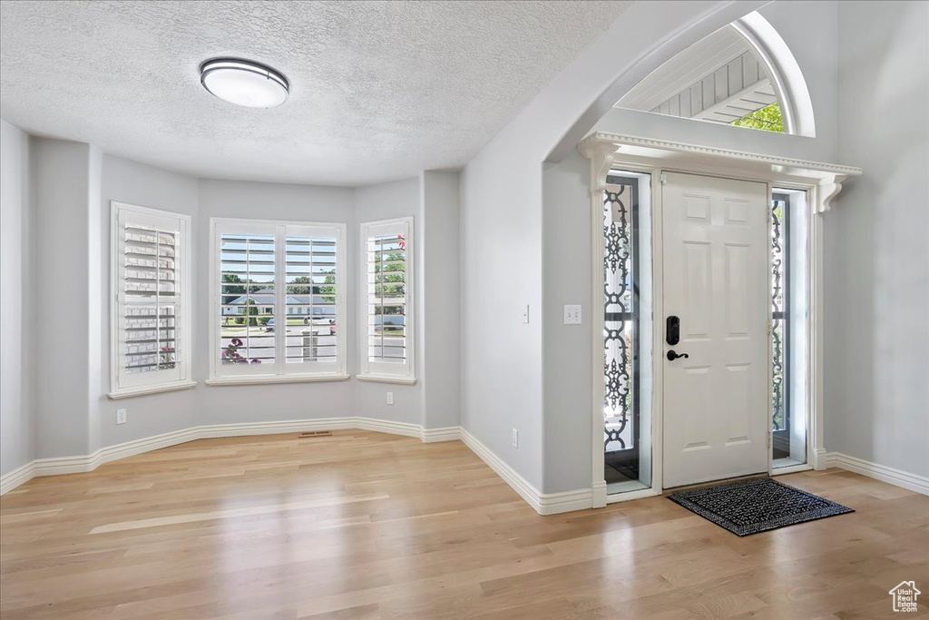 Foyer entrance with wood finished floors, healthy amount of natural light, a textured ceiling, and arched walkways