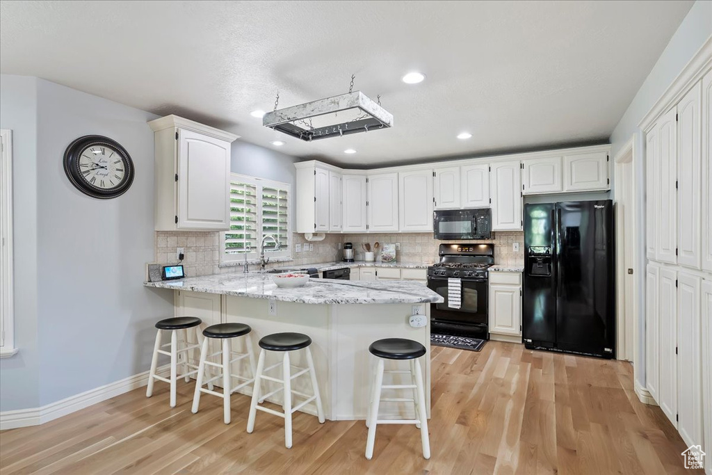 Kitchen featuring black appliances, a peninsula, light wood finished floors, white cabinets, and backsplash