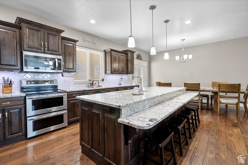 Kitchen with appliances with stainless steel finishes, a chandelier, a breakfast bar, dark brown cabinets, and an island with sink