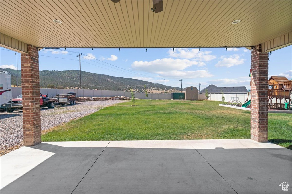 Fenced backyard with a patio area, a shed, a mountain view, and a playground