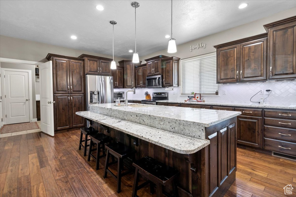 Kitchen with appliances with stainless steel finishes, dark wood finished floors, a kitchen bar, an island with sink, and recessed lighting