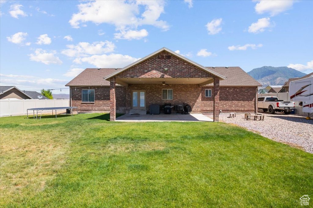 Back of house with a trampoline, brick siding, a patio area, french doors, and a mountain view
