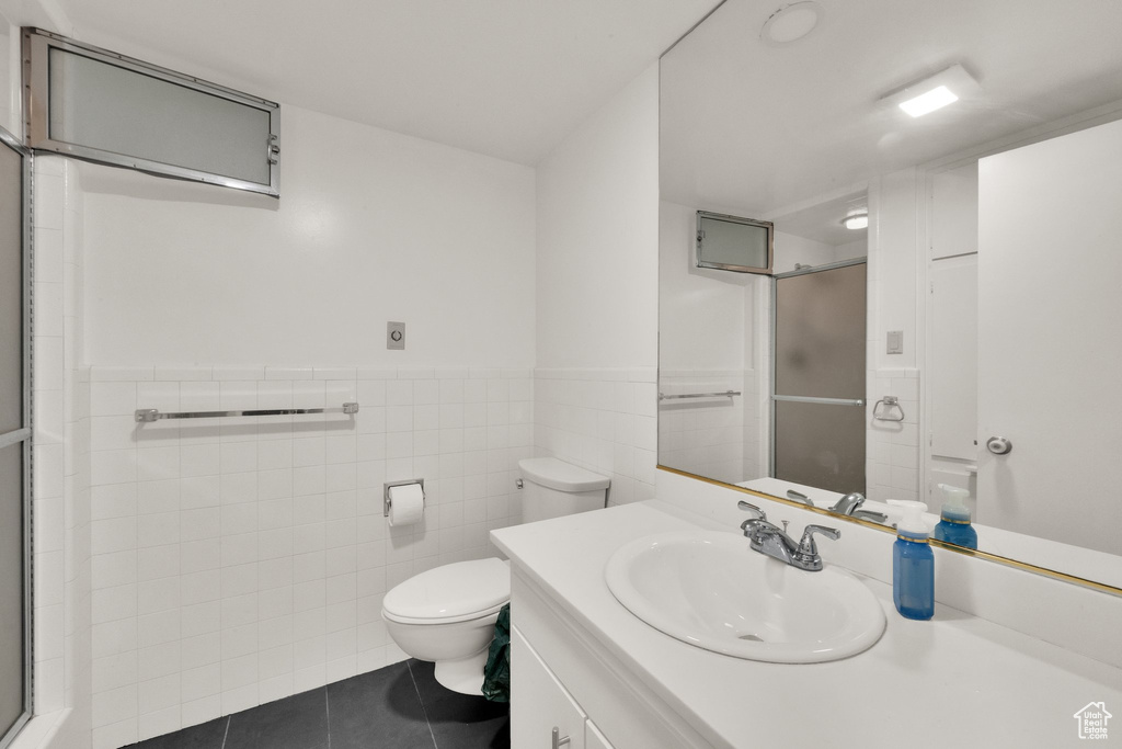 Bathroom featuring tile patterned flooring, a stall shower, vanity, tile walls, and wainscoting