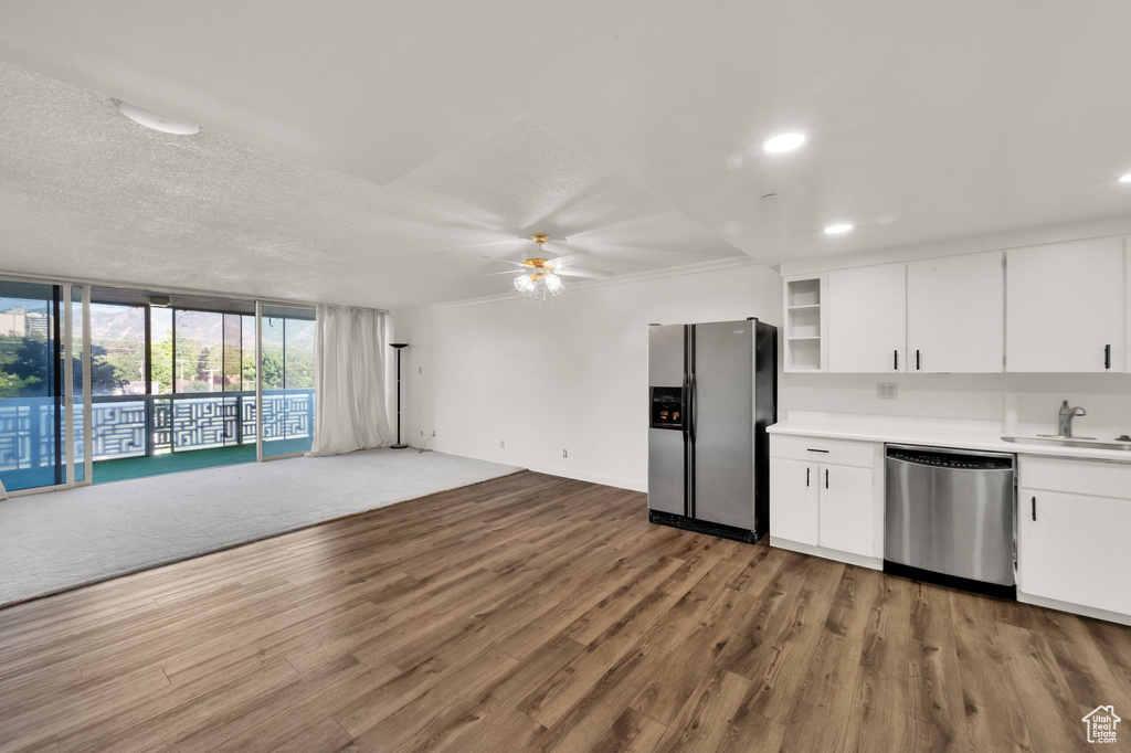 Kitchen with appliances with stainless steel finishes, a ceiling fan, wood finished floors, light countertops, and a wall of windows