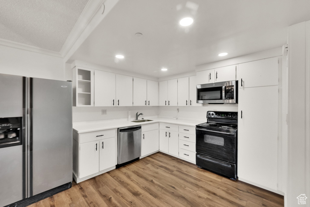 Kitchen featuring appliances with stainless steel finishes, light countertops, white cabinetry, crown molding, and recessed lighting