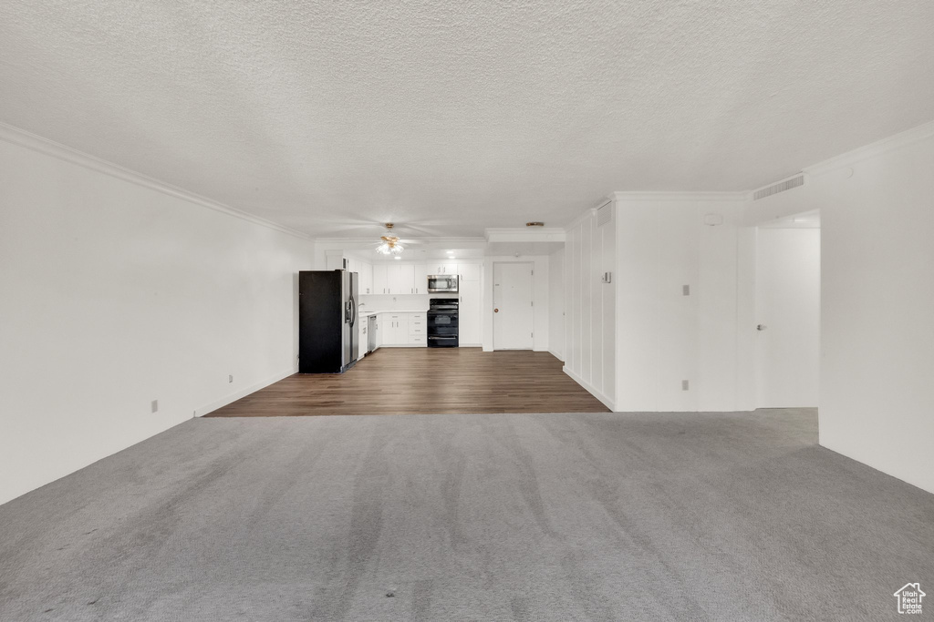 Unfurnished living room featuring dark carpet, a ceiling fan, crown molding, and a textured ceiling