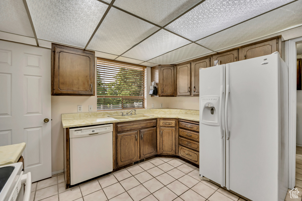 Kitchen featuring white appliances, light countertops, a drop ceiling, and light tile patterned floors