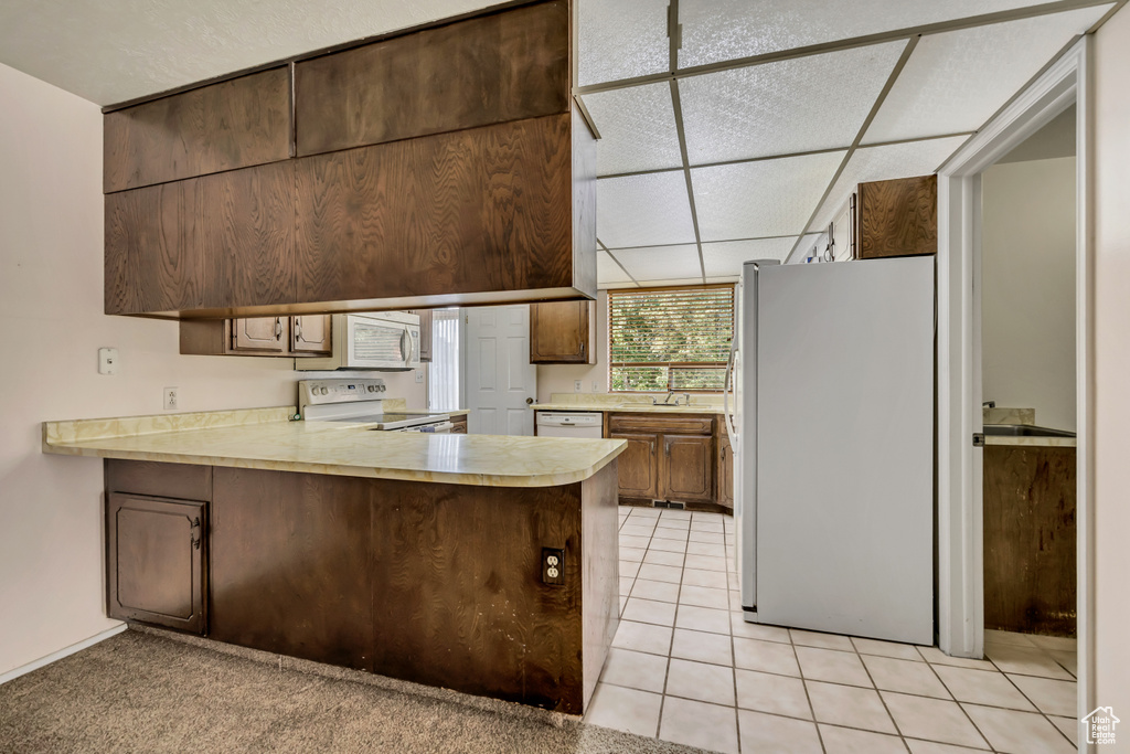 Kitchen featuring white appliances, light countertops, a peninsula, and light tile patterned floors