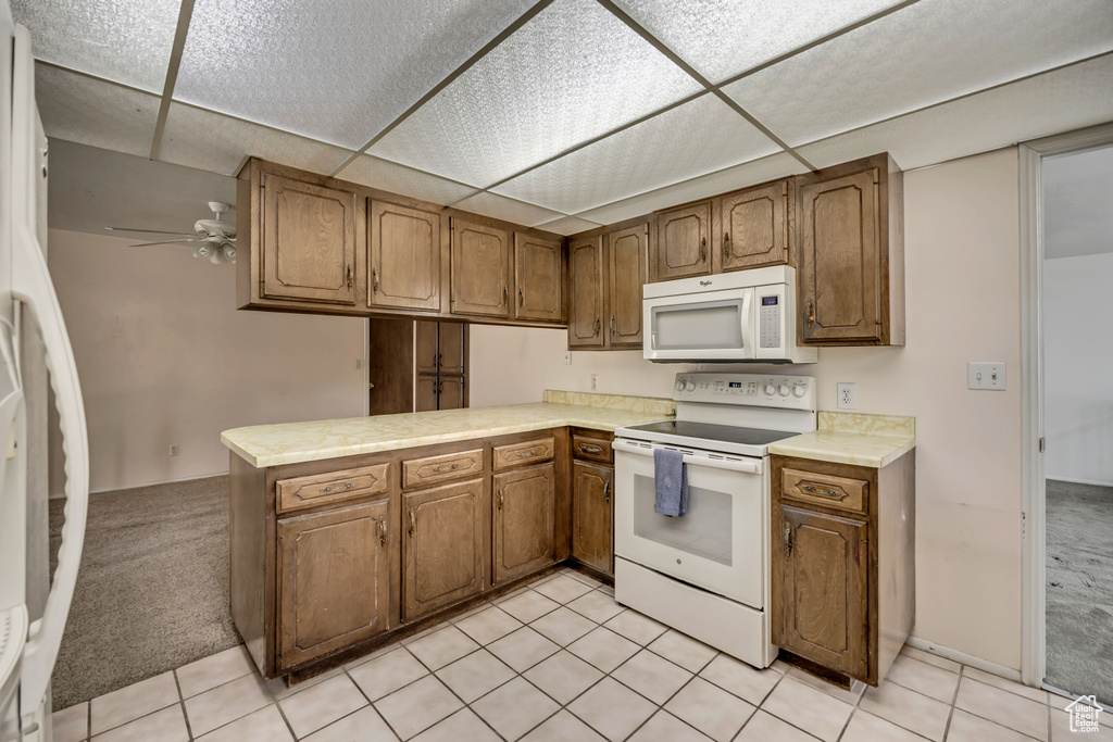 Kitchen with white appliances, a ceiling fan, brown cabinetry, light countertops, and a drop ceiling