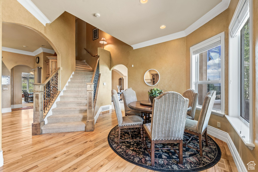Dining space featuring arched walkways, stairs, light wood-style floors, ornamental molding, and recessed lighting