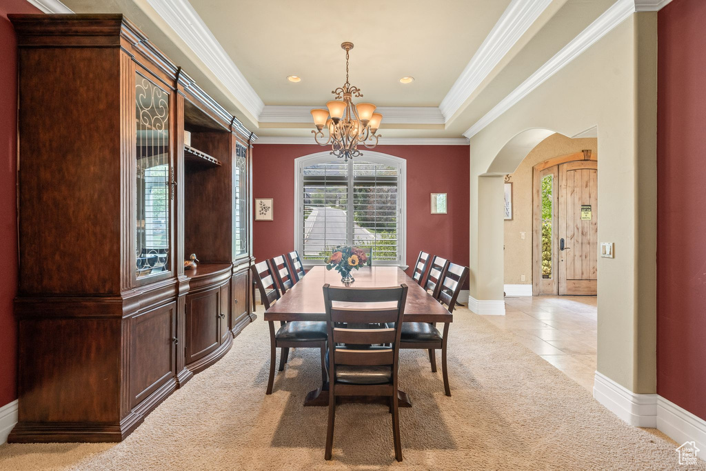 Dining room with a chandelier, arched walkways, crown molding, light carpet, and a raised ceiling