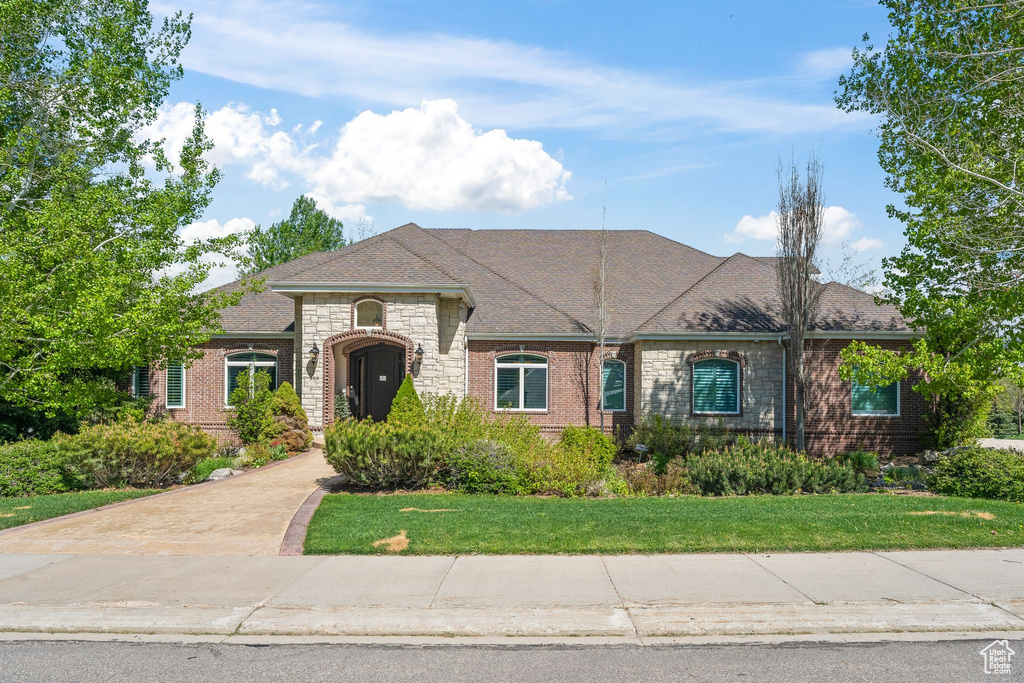 French provincial home with stone siding, a front yard, and roof with shingles
