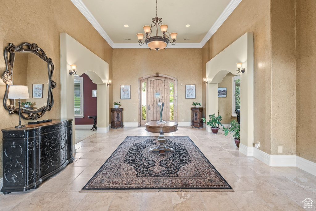 Foyer entrance featuring arched walkways, crown molding, a chandelier, a high ceiling, and recessed lighting