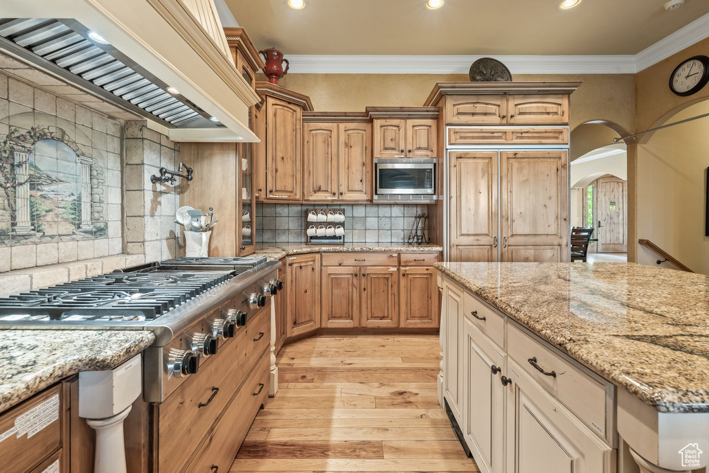 Kitchen featuring appliances with stainless steel finishes, custom exhaust hood, recessed lighting, ornamental molding, and light wood-style floors