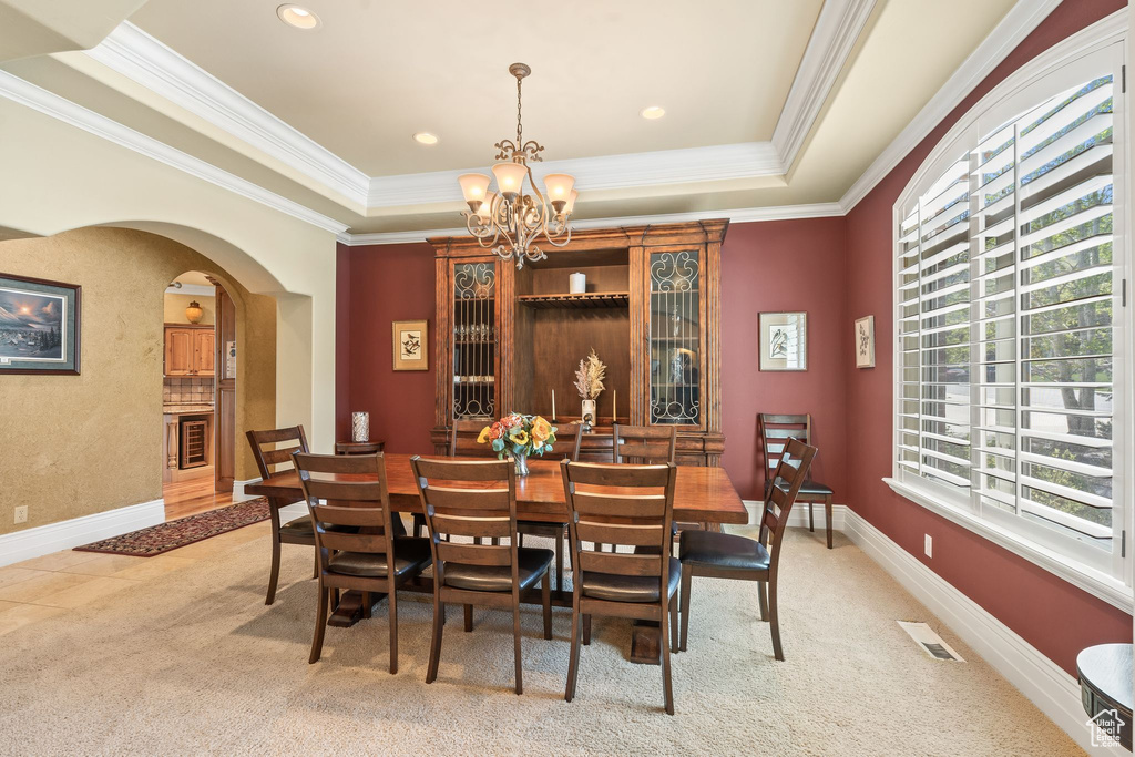 Dining room with arched walkways, a raised ceiling, a chandelier, crown molding, and light carpet