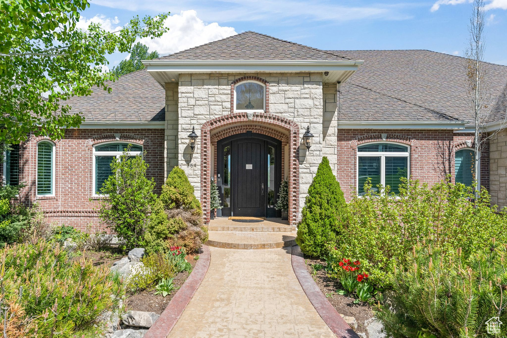 Entrance to property featuring a shingled roof, brick siding, and stone siding