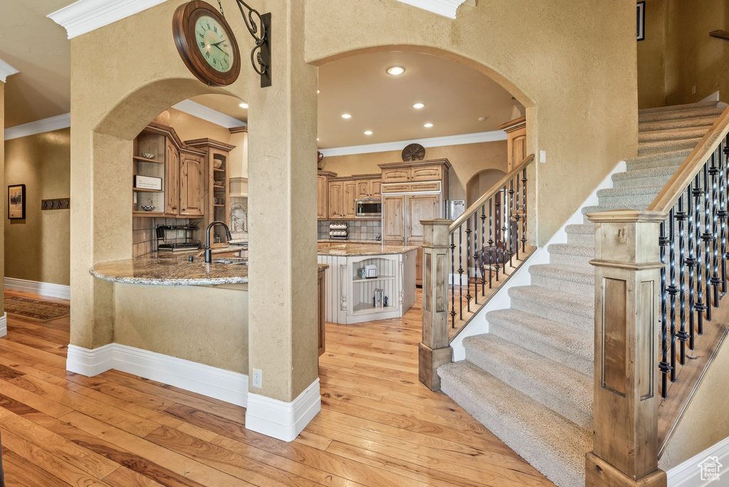 Staircase with crown molding, hardwood / wood-style floors, arched walkways, recessed lighting, and a textured wall