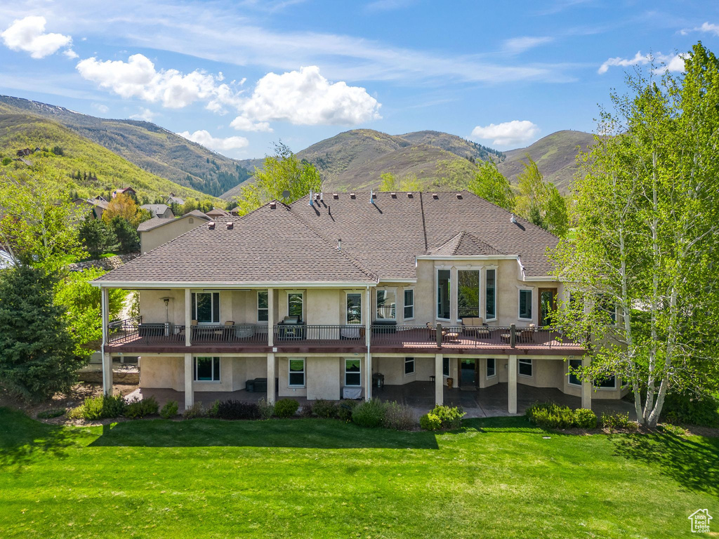 Back of property featuring stucco siding, a patio, a yard, and a deck with mountain view