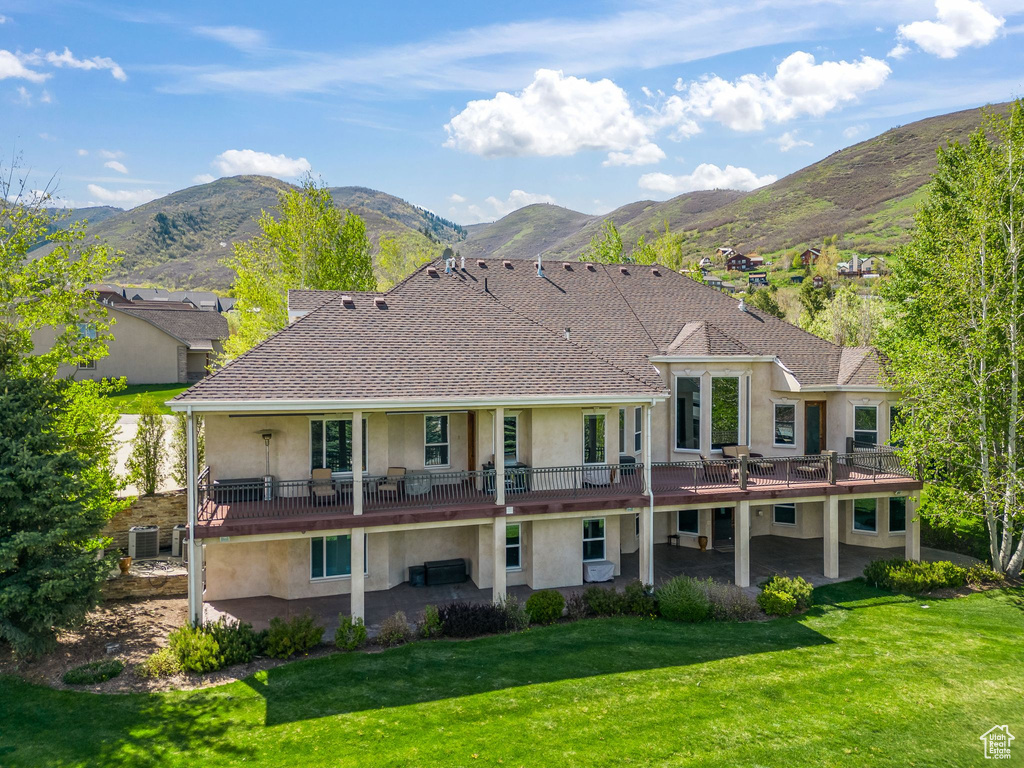 Rear view of property featuring stucco siding, a patio area, a yard, and a deck with mountain view