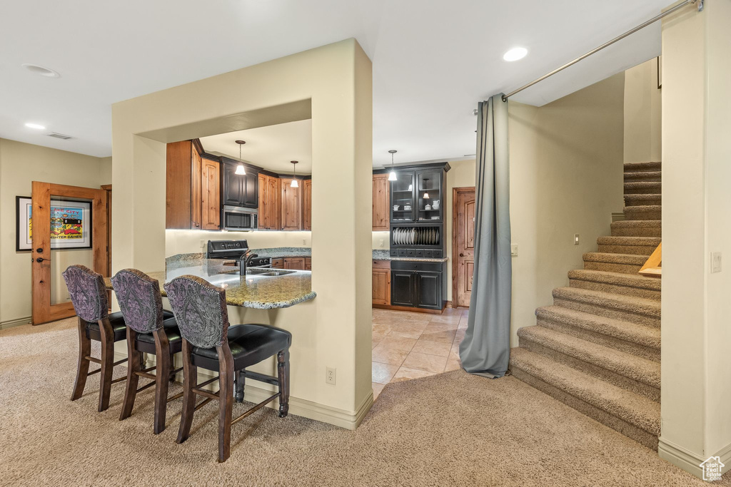 Kitchen with light carpet, stainless steel microwave, a kitchen bar, range, and a peninsula