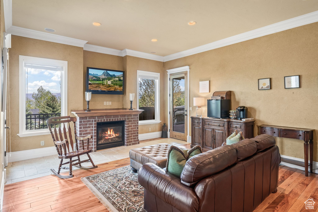 Living room featuring light wood-type flooring, a fireplace, crown molding, and recessed lighting