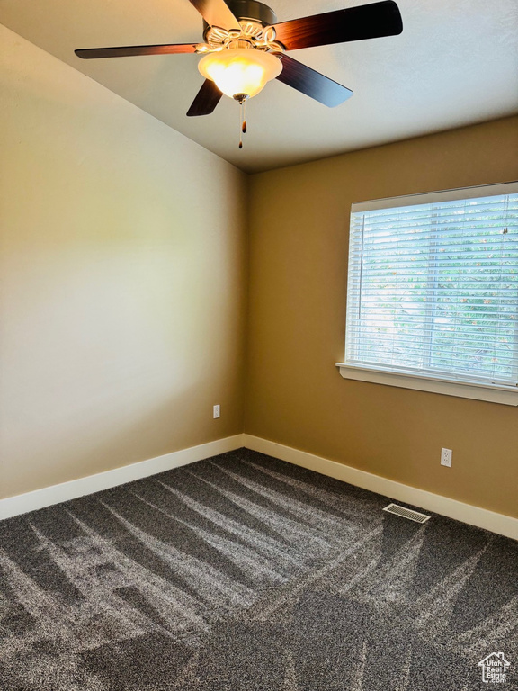 Empty room featuring dark carpet and a ceiling fan