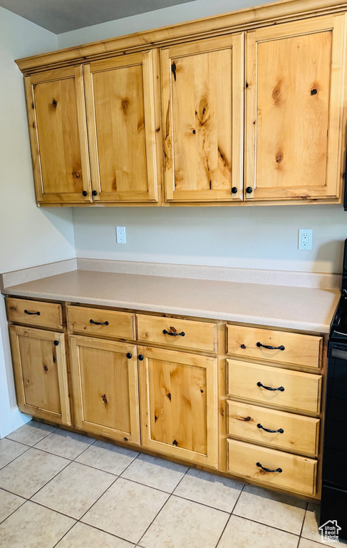 Kitchen with black / electric stove, light countertops, light tile patterned floors, and light brown cabinets