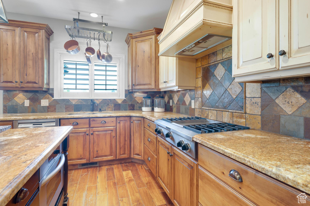 Kitchen featuring stainless steel gas stovetop, custom exhaust hood, light wood-type flooring, backsplash, and brown cabinetry