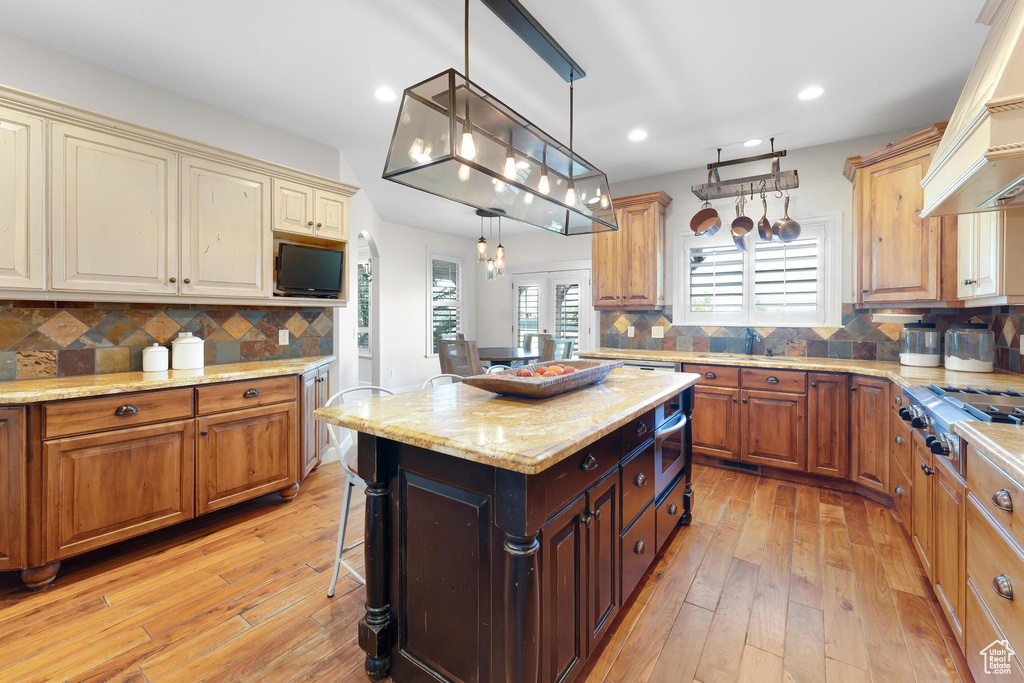 Kitchen featuring stainless steel gas cooktop, light wood finished floors, tasteful backsplash, recessed lighting, and decorative light fixtures