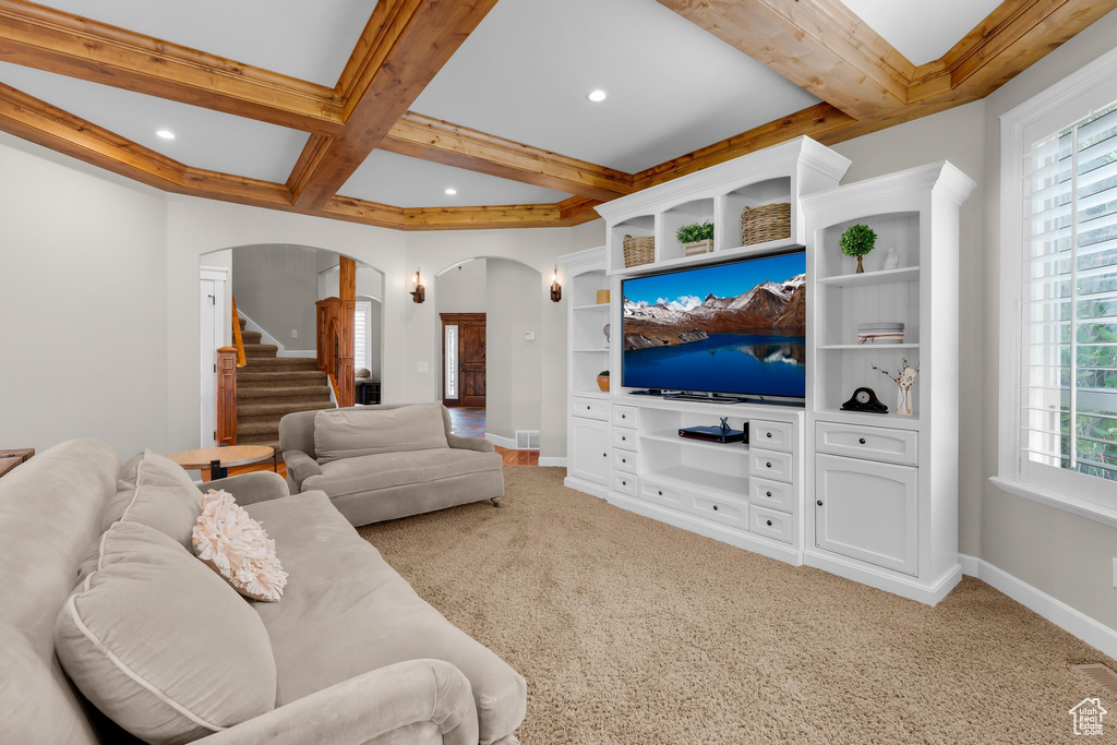Living room with arched walkways, beamed ceiling, light colored carpet, stairway, and coffered ceiling