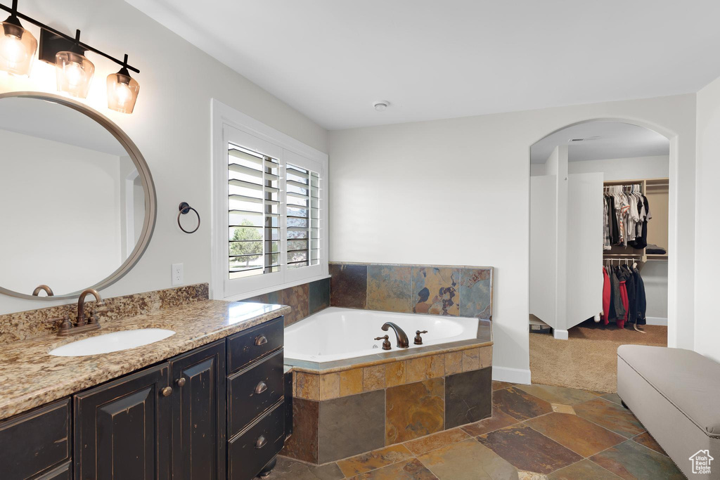 Full bathroom featuring vanity, a garden tub, stone tile floors, and a spacious closet