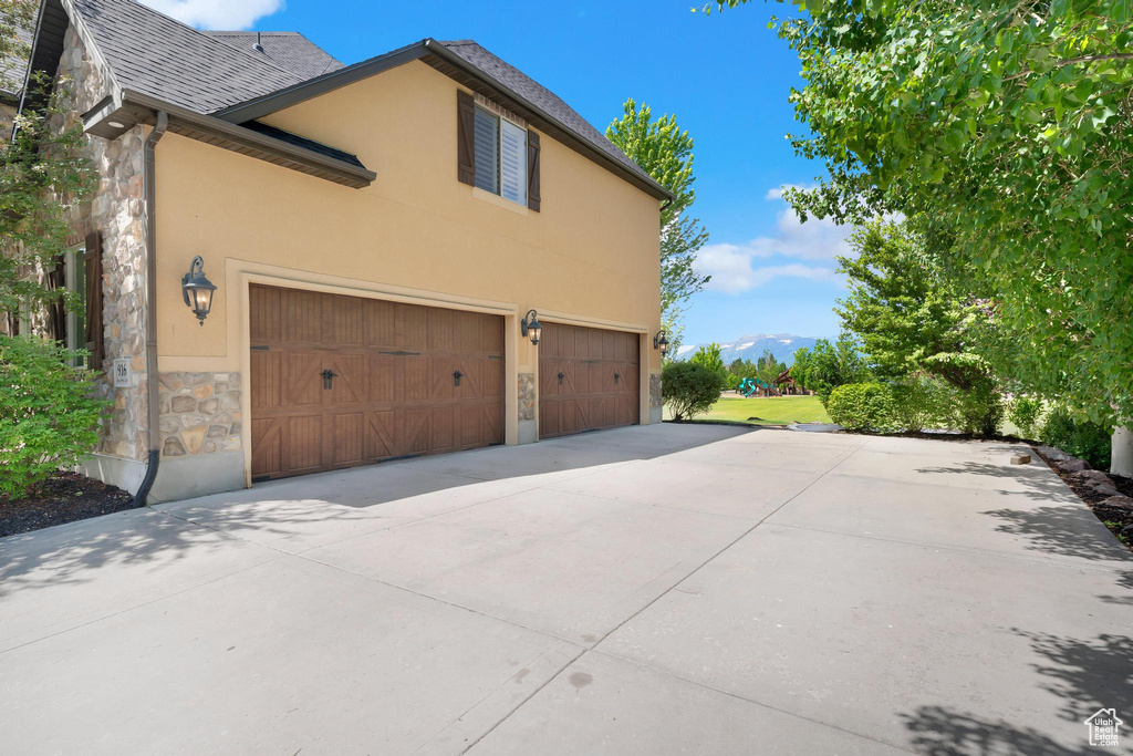 View of side of property with stone siding, a garage, concrete driveway, and stucco siding