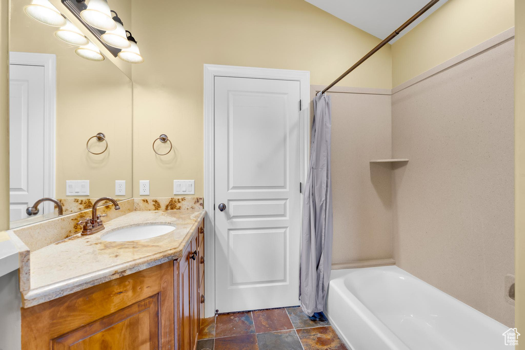 Bathroom with vanity, shower / bath combination with curtain, and stone finish floors