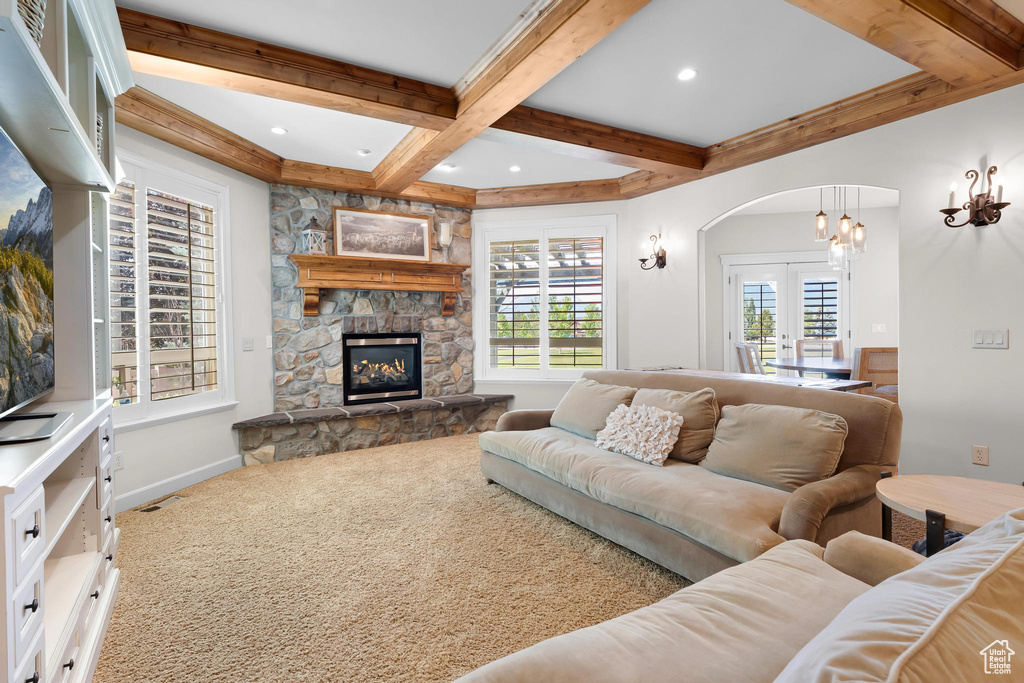 Carpeted living room with beamed ceiling, arched walkways, coffered ceiling, a fireplace, and a chandelier