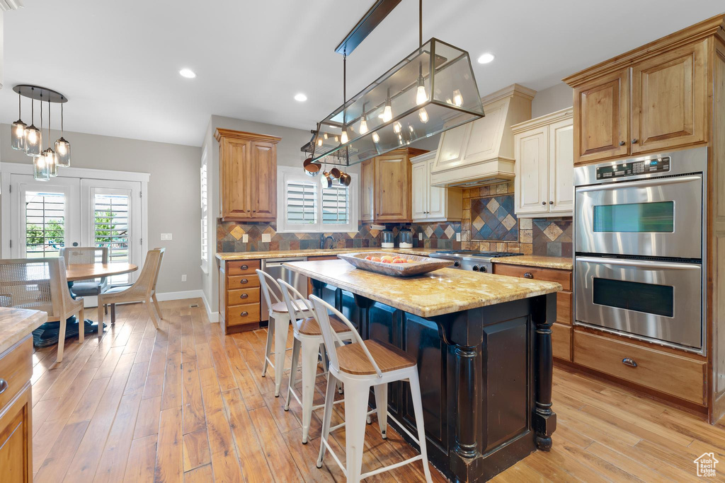 Kitchen featuring appliances with stainless steel finishes, backsplash, a center island, light wood finished floors, and light stone counters
