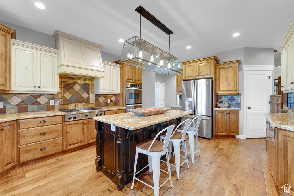 Kitchen with appliances with stainless steel finishes, tasteful backsplash, a breakfast bar, light wood finished floors, and light stone countertops