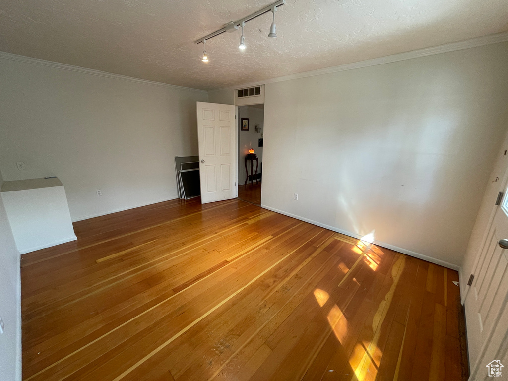 Unfurnished bedroom with track lighting, hardwood / wood-style floors, a textured ceiling, and crown molding