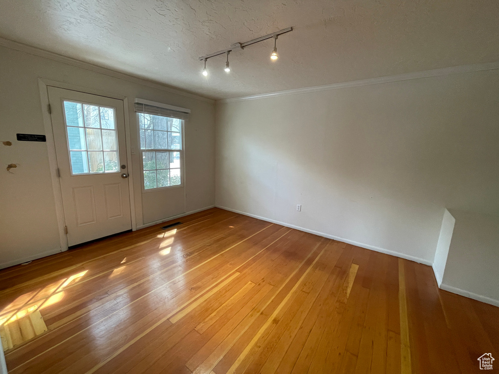 Unfurnished room featuring rail lighting, crown molding, light wood-style flooring, and a textured ceiling