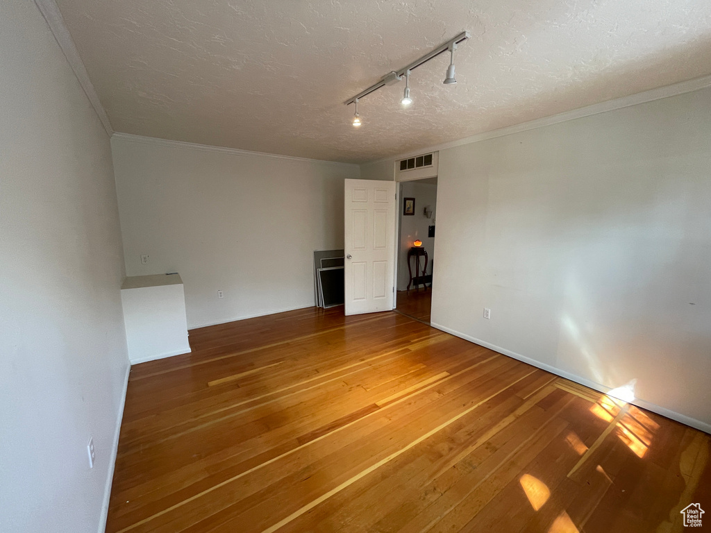 Unfurnished room featuring track lighting, hardwood / wood-style floors, a textured ceiling, and ornamental molding