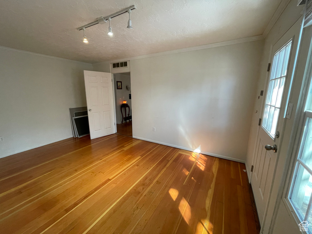 Unfurnished room featuring light wood-style flooring, rail lighting, plenty of natural light, a textured ceiling, and ornamental molding