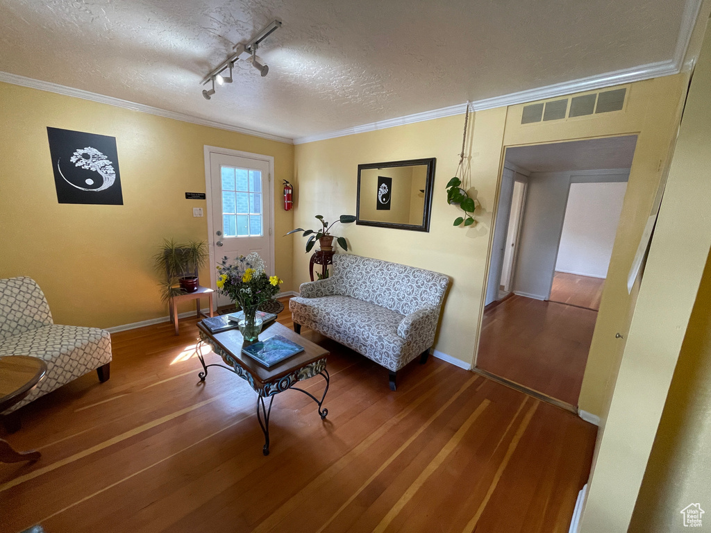 Living room with wood finished floors, a textured ceiling, crown molding, and rail lighting