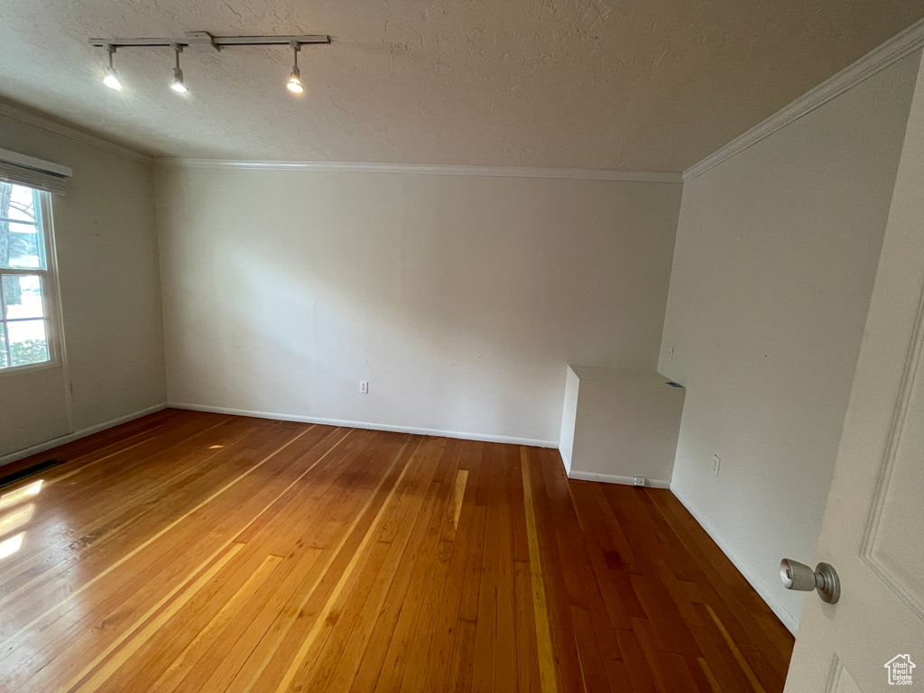 Empty room featuring hardwood / wood-style floors, track lighting, a textured ceiling, and crown molding