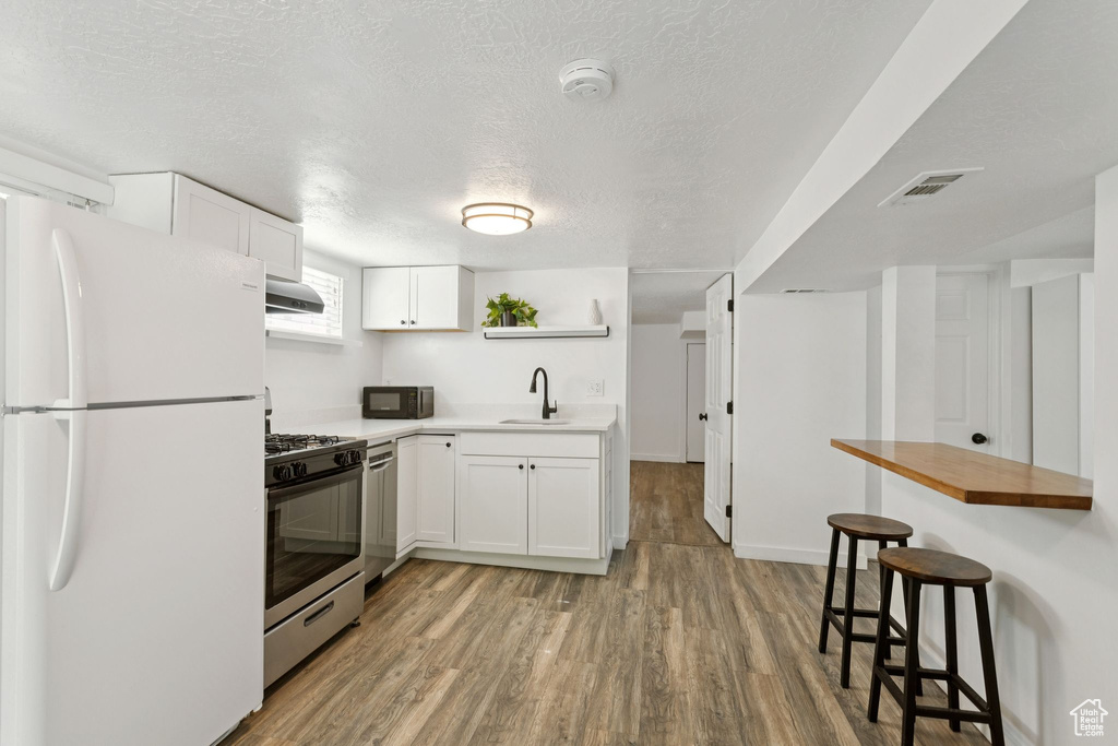 Kitchen featuring freestanding refrigerator, stainless steel gas range oven, black microwave, light wood-type flooring, and a breakfast bar
