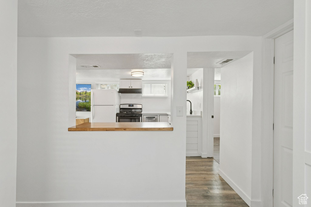 Kitchen featuring freestanding refrigerator, gas range, under cabinet range hood, dark wood finished floors, and a peninsula