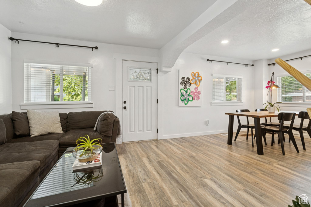 Living room with light wood-type flooring, a textured ceiling, recessed lighting, and arched walkways