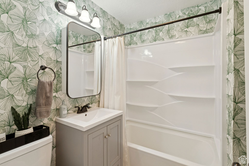 Full bath featuring wallpapered walls, vanity, and shower / tub combo